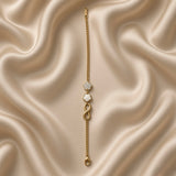 Gold Infinity Clover Crystal Flower Charm Bracelet Curb Chain - circular flat lay on cream satin: bold gold curb chain with three cascading charms at top — white crystal pave flower, white enamel quatrefoil clover, bold 3D gold infinity, flat gold ID bar tag and lobster clasp at bottom