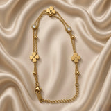 Gold Clover and Crystal Station Bracelet Satellite Chain - circular flat lay on cream satin: full bracelet loop showing all nine stations, three flat gold clover stations at top centre, two round crystal bezel stations symmetrically placed, four small gold ball satellites on cable chain, lobster clasp with engraved gold bar tag at bottom left, curb extender chain at right