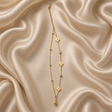 Gold Clover and Crystal Station Bracelet Satellite Chain - vertical flat lay on cream satin: fine gold cable chain with nine inline stations, three flat mirror-polish gold four-petal clover stations clustered at centre, two round white crystal zirconia bezel stations at outer positions, four small gold ball satellites flanking crystal bezels, lobster clasp at base with curb extender chain at top
