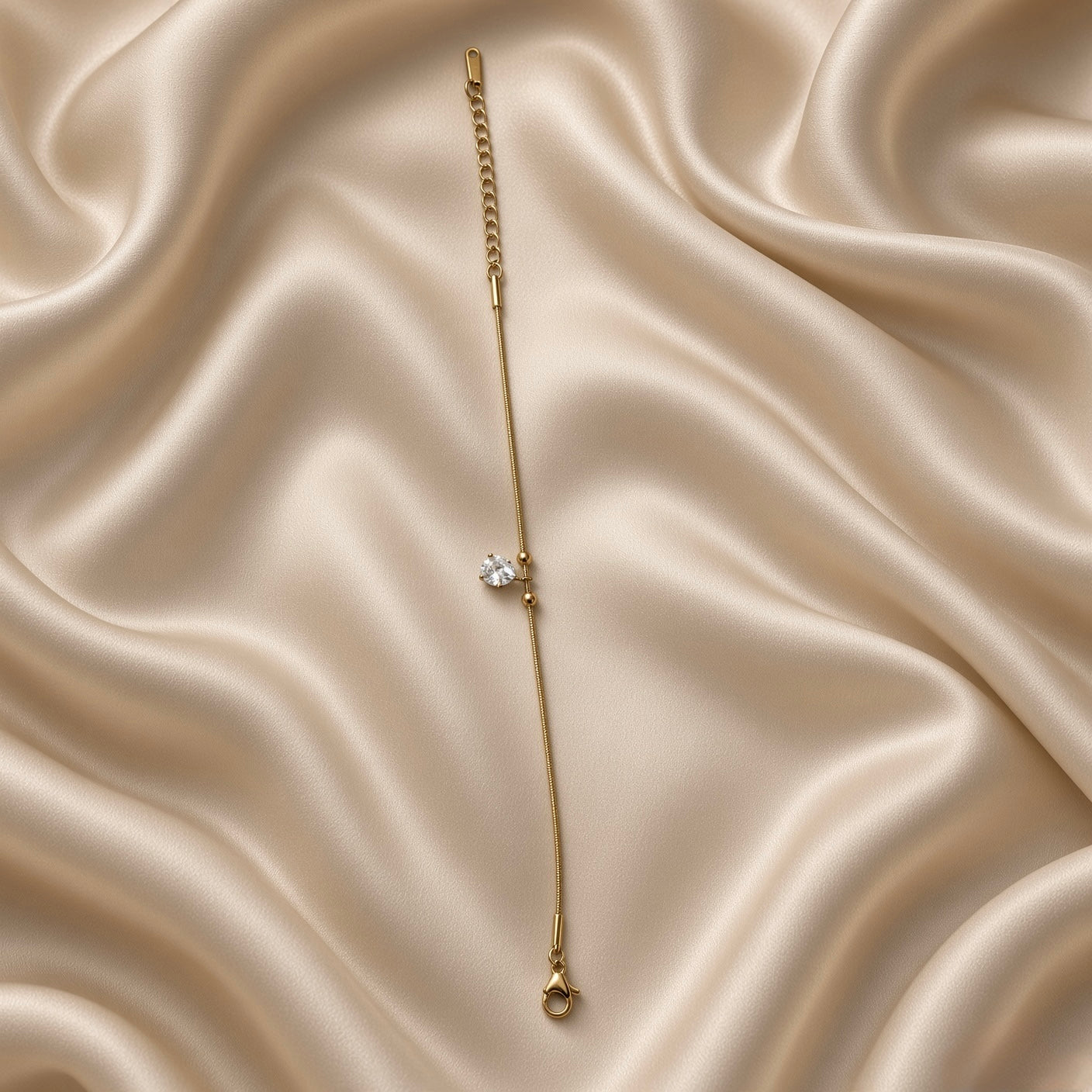 Pear Crystal Solitaire Drop Bracelet Snake Chain Gold - extreme macro on cream satin: pear-cut brilliant white crystal zirconia solitaire in four-prong gold claw setting in close detail, two smooth gold ball satellites on ribbed snake chain on each side, pure colourless diamond-like white brilliance and facet detail clearly visible