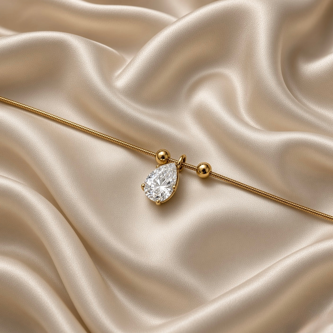 Pear Crystal Solitaire Drop Bracelet Snake Chain Gold - vertical flat lay on cream satin: smooth ribbed round gold snake chain with single pear-cut white crystal zirconia solitaire drop pendant flanked by two gold ball satellites at centre, lobster clasp at base, curb extender chain at top
