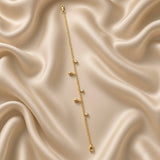 Gold Raindrop and Crystal Bezel Station Bracelet - circular flat lay on cream satin showing full bracelet loop: five alternating charms visible — two solid mirror-polish gold raindrop charms and three round white crystal zirconia bezel drop charms on fine gold cable chain, lobster clasp with gold barrel connector at bottom