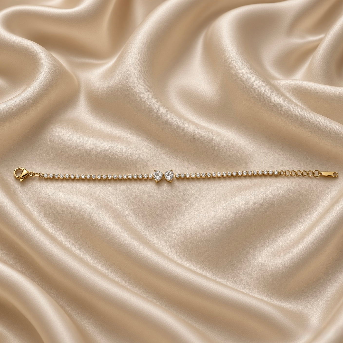 Double Pear Crystal Tennis Bracelet Gold Round Bezel - close vertical flat lay on cream satin: second angle of full tennis chain showing continuous round brilliant crystal bezel stations in warm gold, double pear white crystal zirconia accent at centre, rounded tops touching and pointed tips descending in double teardrop composition