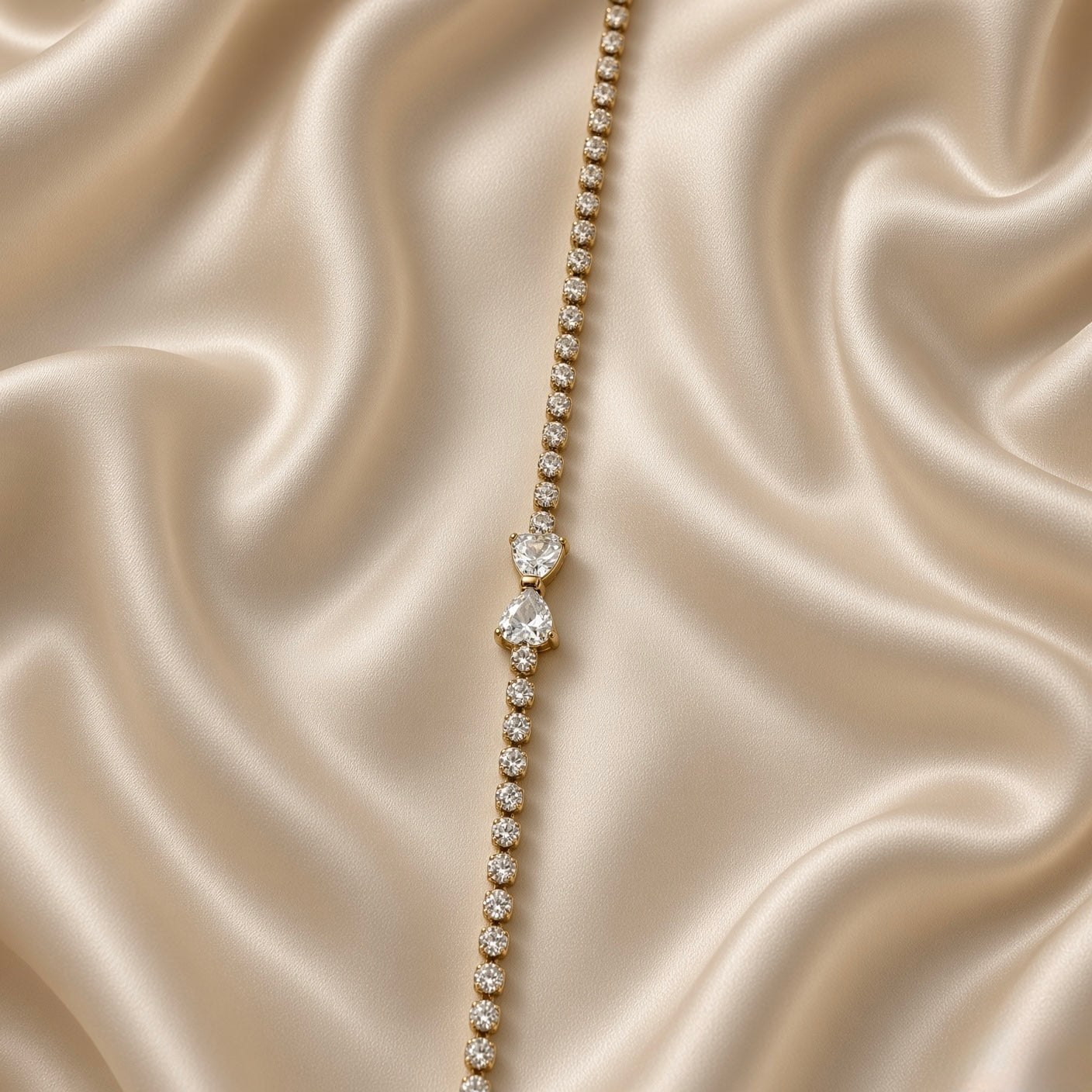 Double Pear Crystal Tennis Bracelet Gold Round Bezel - full horizontal flat lay on cream satin: complete bracelet laid straight showing full length of round brilliant crystal tennis chain, double pear crystal centre accent at midpoint, lobster clasp at left end, curb extension chain with flat bar tag at right end for adjustable fit
