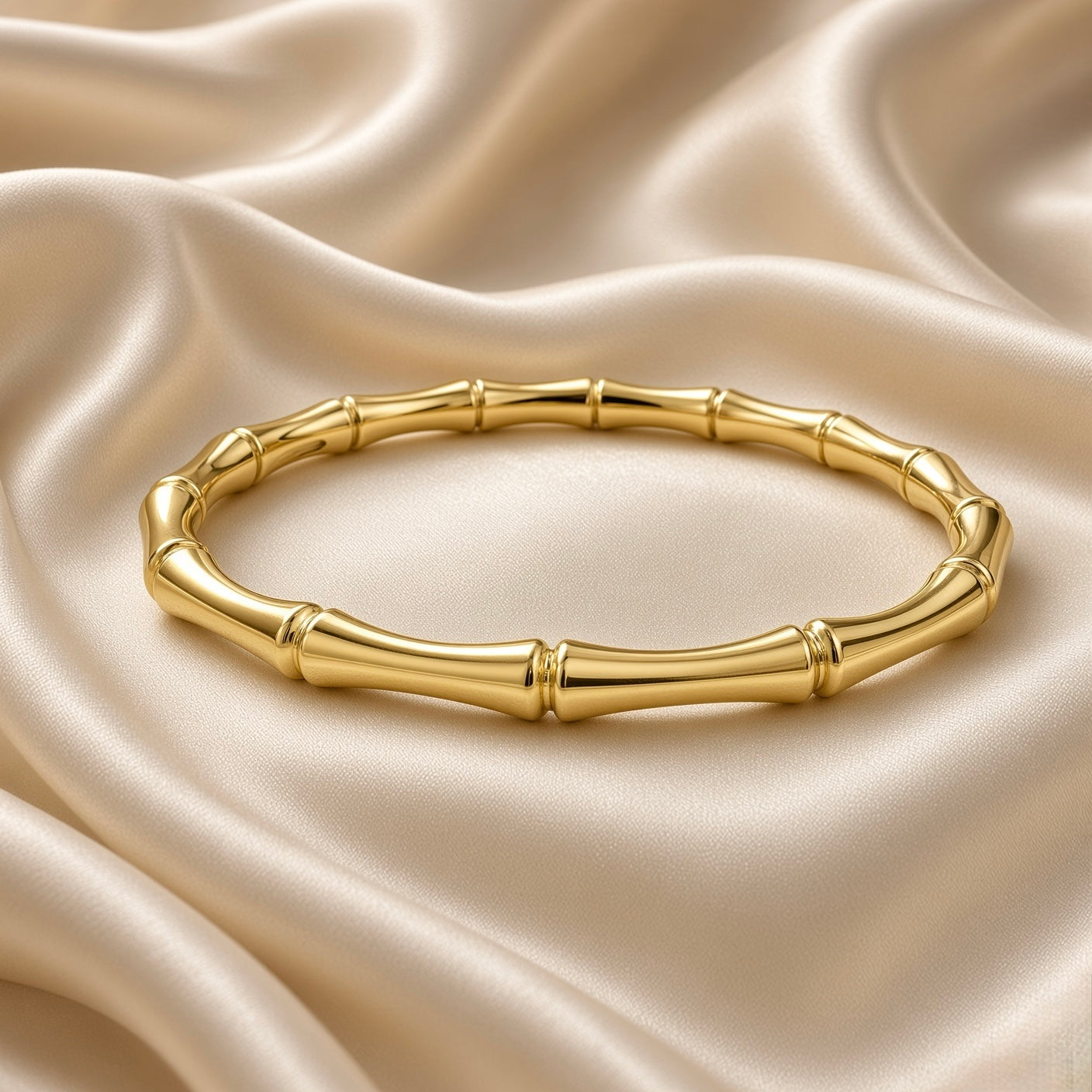 Gold Bamboo Bangle Bracelet Mirror Polish Sculptural - on wrist lifestyle: bangle worn on elegant wrist with white sleeve, bamboo motif tube sections and double-ring node joints visible in warm mirror-polish gold wrapping wrist, hinge gap visible at top, slim elegant wrist profile, white satin background