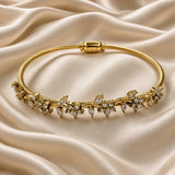 Gold Twisted Wire Bangle Floral Marquise Crystal Garland Magnetic Clasp - on wrist lifestyle: bangle worn on elegant wrist with white satin sleeve, floral marquise and round crystal garland wrapping wrist front in continuous botanical vine of sparkling white crystal zirconia in warm gold prong settings, twisted wire visible at wrist sides and back, white satin background