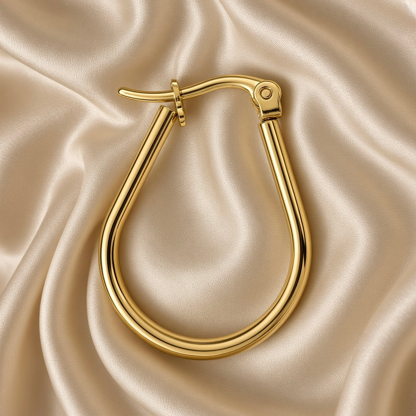 Gold Teardrop Hoop Earrings Tube Round Section Mirror Polish Latch Back Clasp - angled pair flat lay on cream satin: pair of teardrop tube hoops shown overlapping at alternate angle, full round-section tubular hoop body visible in warm 18K gold mirror-polish finish, clasp detail and barrel hinge at top of each hoop, complete teardrop silhouette from each earring visible, cream satin background