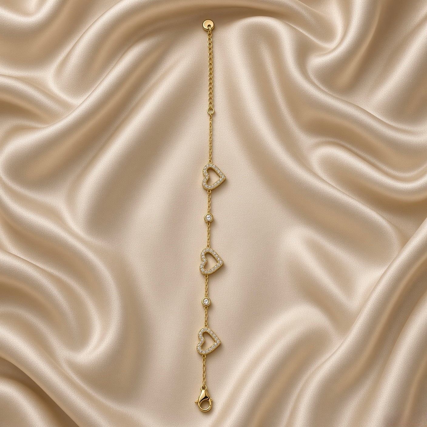 Gold Open Pavé Heart Charm Bracelet Bezel Crystal Station Chain - vertical detail flat lay on cream satin: straight layout showing full heart charm and bezel station sequence in alternating heart-station-heart-station-heart arrangement on fine warm gold cable chain, micro-pavé white crystal detail on each open heart frame visible, cream satin background