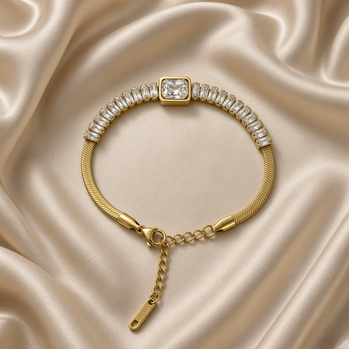 Gold Herringbone Chain Bracelet Baguette Crystal Station Emerald Bezel Centre - overhead circular flat lay on cream satin: full bracelet in circular form showing complete herringbone chain body, full baguette crystal channel row, large emerald bezel centre at top, lobster clasp and adjustable curb link extension chain at bottom, cream satin background