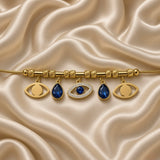 Gold Evil Eye Charm Bracelet Blue Crystal Teardrop Pavé Nazar Snake Chain - hero overhead flat lay on cream satin: full bracelet in circular form on snake chain with bead stations, 5 charms displayed: 2 open plain gold eye charms at outer positions, 2 deep sapphire blue pear-cut teardrop crystal charms in warm gold bezel, 1 central large pavé white crystal marquise evil eye charm with blue round crystal centre, cream satin background