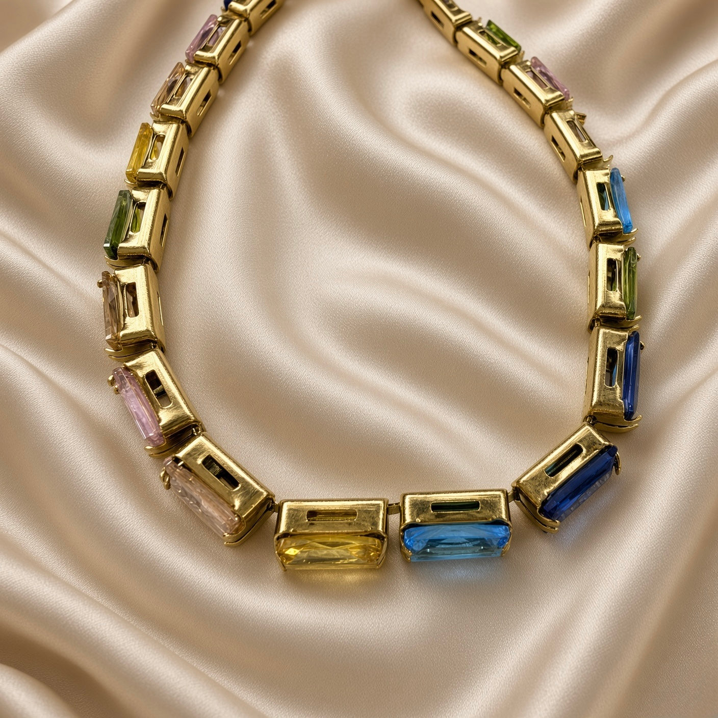 Gold Multi-Colour Emerald Cut Crystal Tennis Bracelet Bolo Adjustable Slider - extended flat lay on cream satin: bracelet fully extended in straight drape showing bolo slider mechanism at top with two warm gold box chain tails and gold ball tips forming V shape, complete continuous multi-colour emerald-cut crystal tennis line at bottom, cream satin background