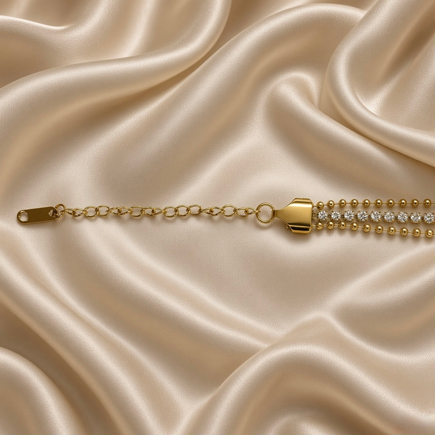 Gold Three Row Bracelet Crystal Tennis Centre Ball Bead Chain Lobster Clasp - on wrist lifestyle: bracelet worn on warm-toned wrist with white satin sleeve, wide three-row construction sitting across wrist showing smooth upper and lower warm gold ball bead rows flanking centre round brilliant white crystal tennis row, tapered shield end cap and extension chain at wrist side, white satin background
