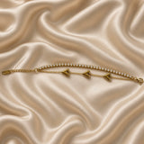 Gold Double Strand Bracelet Crystal Tennis Row Triple Puffy Heart Charm Chain - hero overhead flat lay on cream satin: full bracelet extended horizontally showing upper continuous round brilliant white crystal zirconia tennis strand edge-to-edge and lower fine warm gold cable chain with three evenly spaced fully three-dimensional mirror-smooth warm gold puffy heart charms, warm gold jump ring end connectors, lobster clasp at right, cream satin background