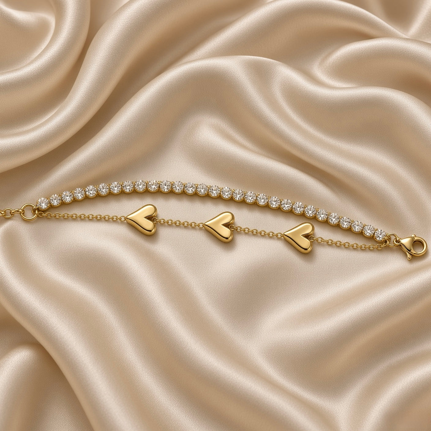 Gold Double Strand Bracelet Crystal Tennis Row Triple Puffy Heart Charm Chain - full extended flat lay on cream satin: bracelet fully extended showing complete double-strand construction from adjustable curb link extension chain with small flat engraved warm gold tag at left to lobster clasp at right, upper continuous crystal tennis row and lower triple puffy heart charm cable chain in full parallel length, cream satin background