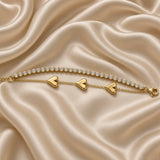 Gold Double Strand Bracelet Crystal Tennis Row Triple Puffy Heart Charm Chain - full extended flat lay on cream satin: bracelet fully extended showing complete double-strand construction from adjustable curb link extension chain with small flat engraved warm gold tag at left to lobster clasp at right, upper continuous crystal tennis row and lower triple puffy heart charm cable chain in full parallel length, cream satin background