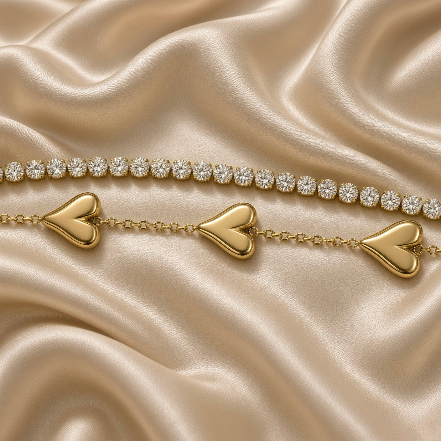 Gold Double Strand Bracelet Crystal Tennis Row Triple Puffy Heart Charm Chain - macro detail flat lay on cream satin: extreme close-up showing upper round brilliant white crystal zirconia tennis row with individually cup-set stones edge-to-edge and lower strand with three volumetric mirror-smooth domed warm gold puffy heart charms with heart cleft at top, fine warm gold cable chain between hearts, warm gold sculptural detail of puffy heart surfaces visible, cream satin background
