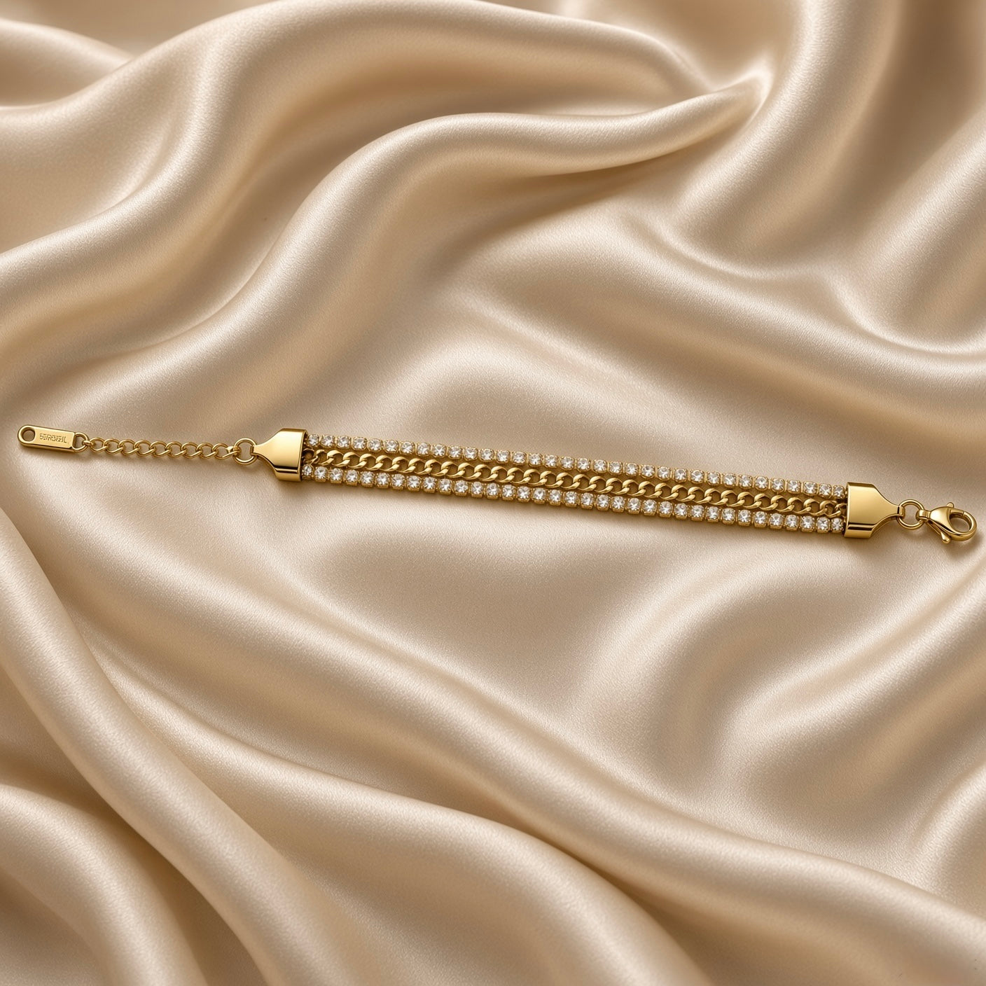 Gold Cuban Link Chain Bracelet Double Crystal Tennis Row Three Row Shield Clasp - full length extended flat lay on cream satin: bracelet fully extended showing tapered shield end cap on left with adjustable curb link extension chain and engraved flat rectangular tag, complete three-row body, lobster clasp at right end, cream satin background