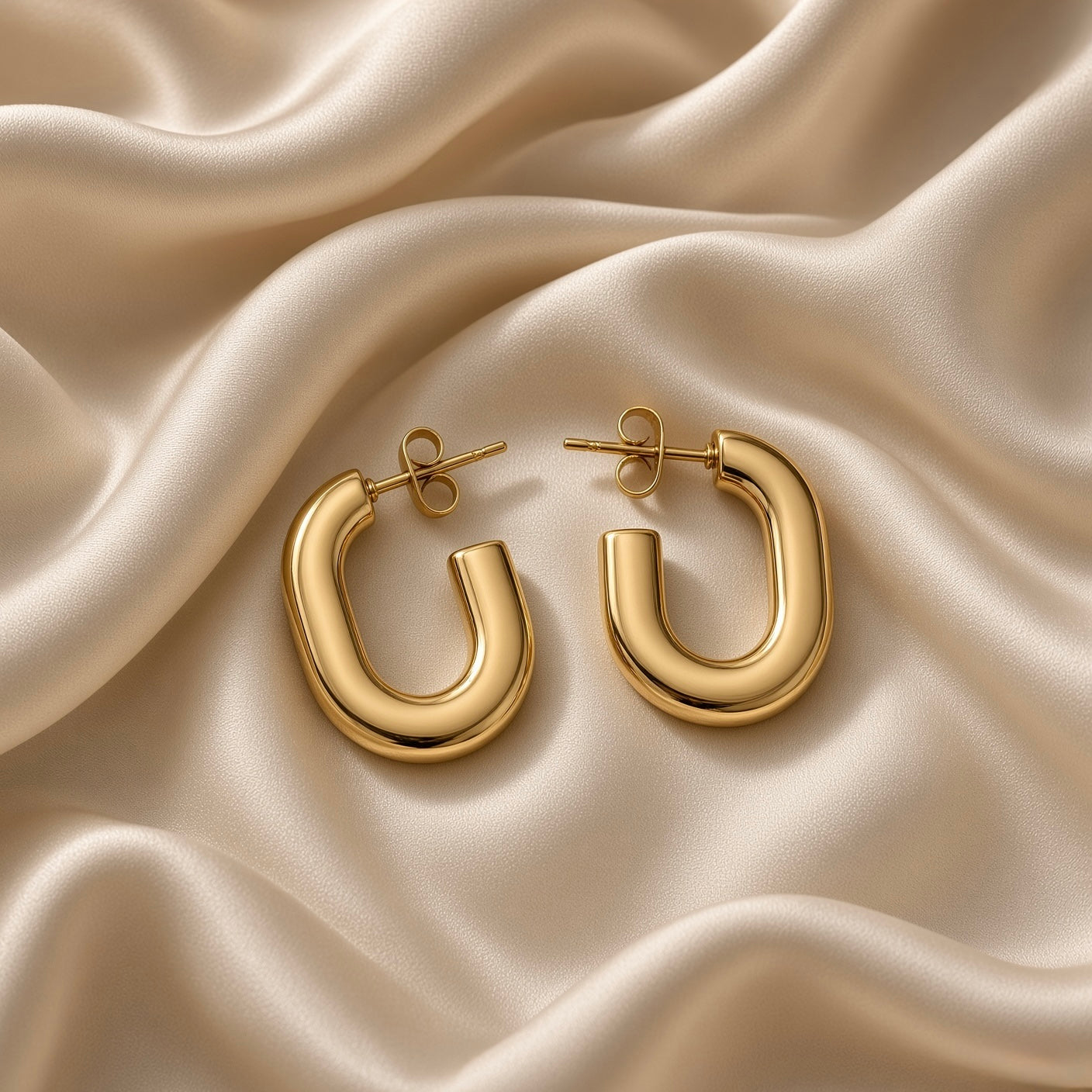 Close-up of a polished gold-tone U-shaped hoop earring on champagne satin