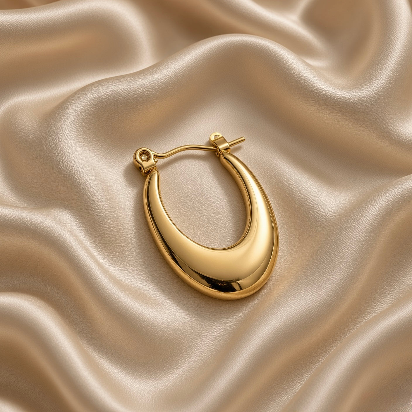 Gold-tone teardrop hoop earring worn on an ear