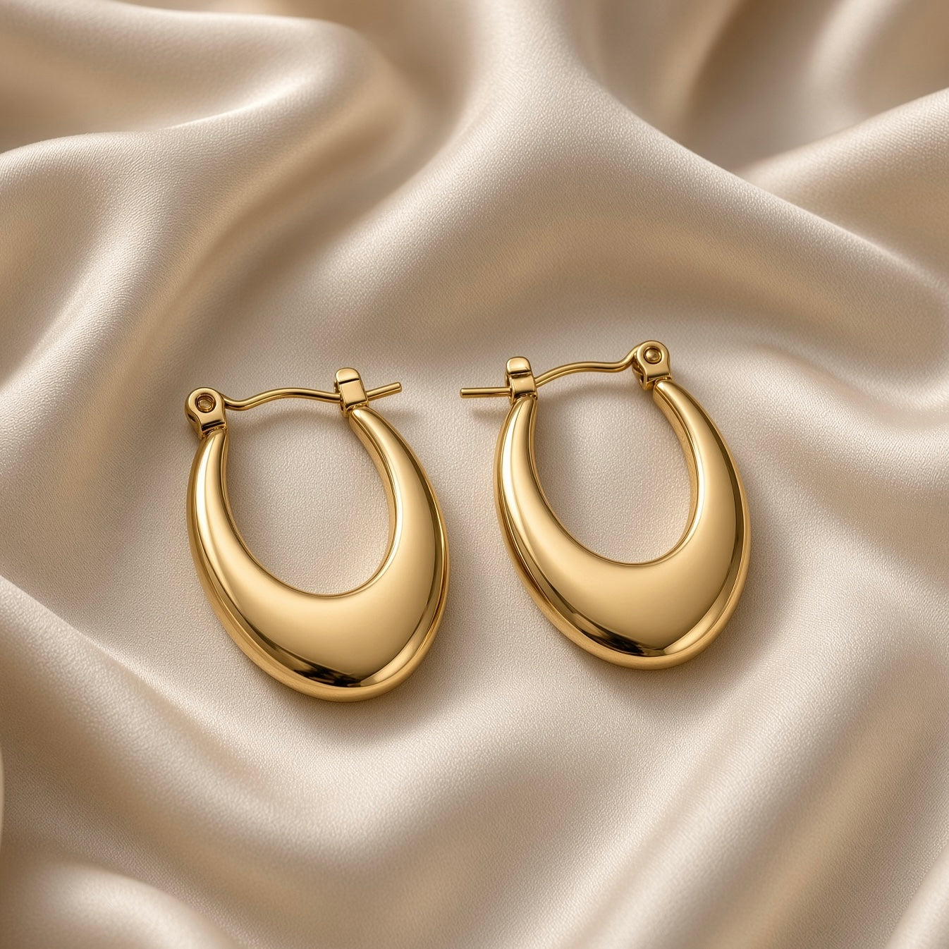 Pair of polished gold-tone teardrop hoop earrings on champagne satin