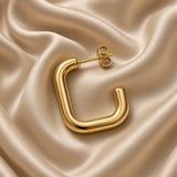 Close-up of one polished gold-tone square U-shaped hoop earring and butterfly back on champagne satin
