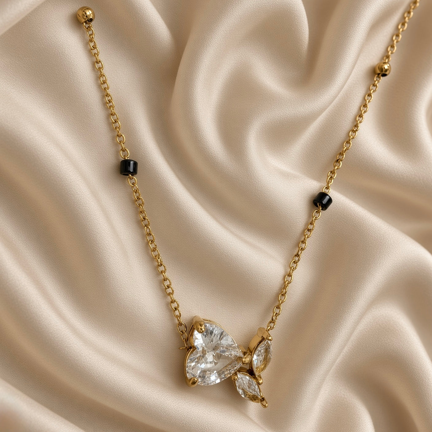 Full view of gold-tone necklace with black bead accents and heart butterfly pendant on cream satin