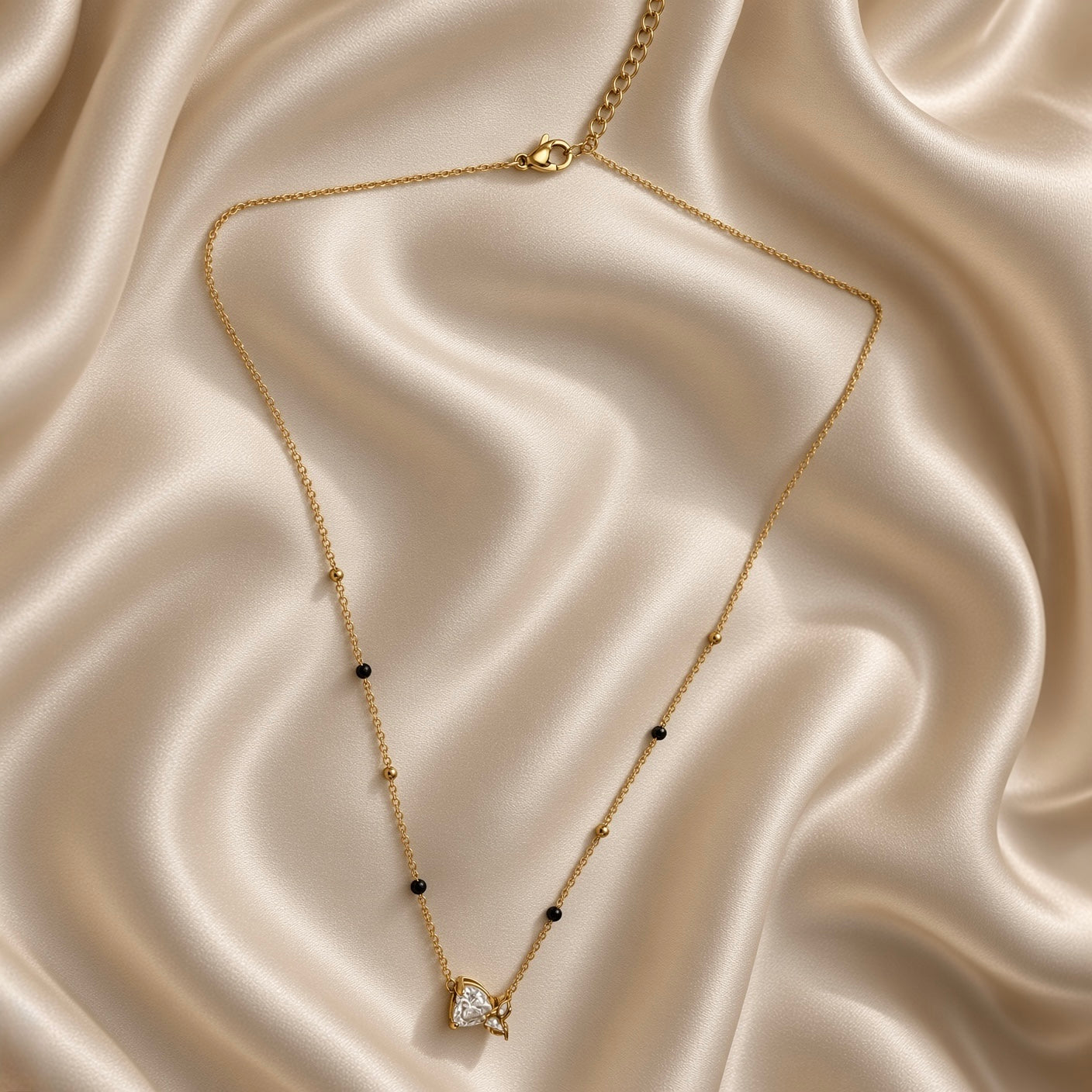 Gold-tone chain necklace with black bead accents and clear heart butterfly pendant on satin