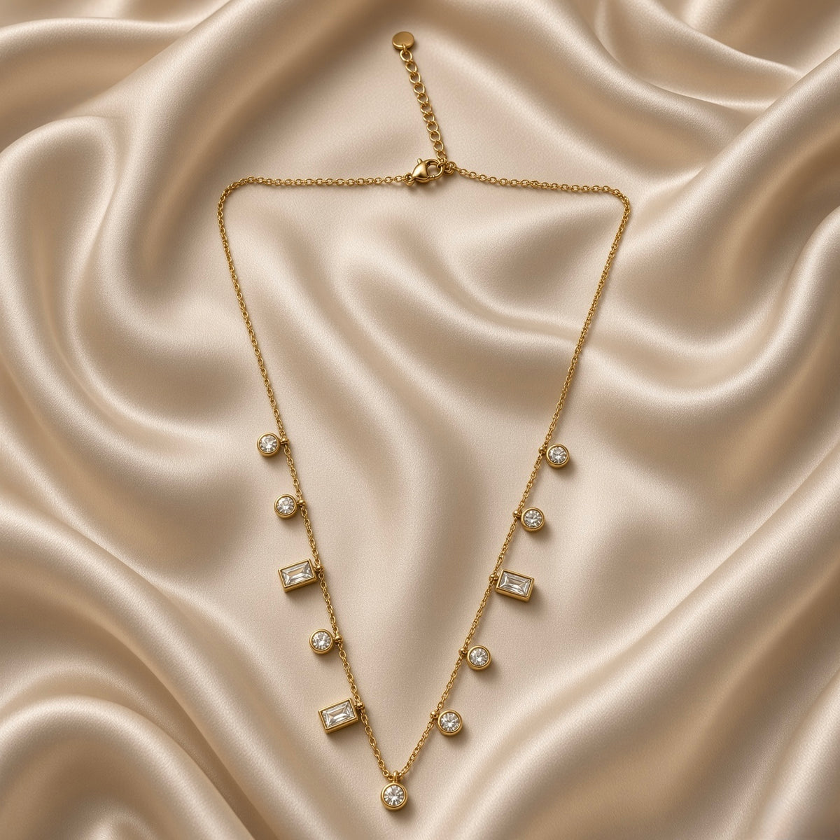 Full view of gold-tone station necklace with round and rectangular clear stones on cream satin