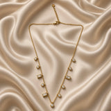 Full view of gold-tone station necklace with round and rectangular clear stones on cream satin