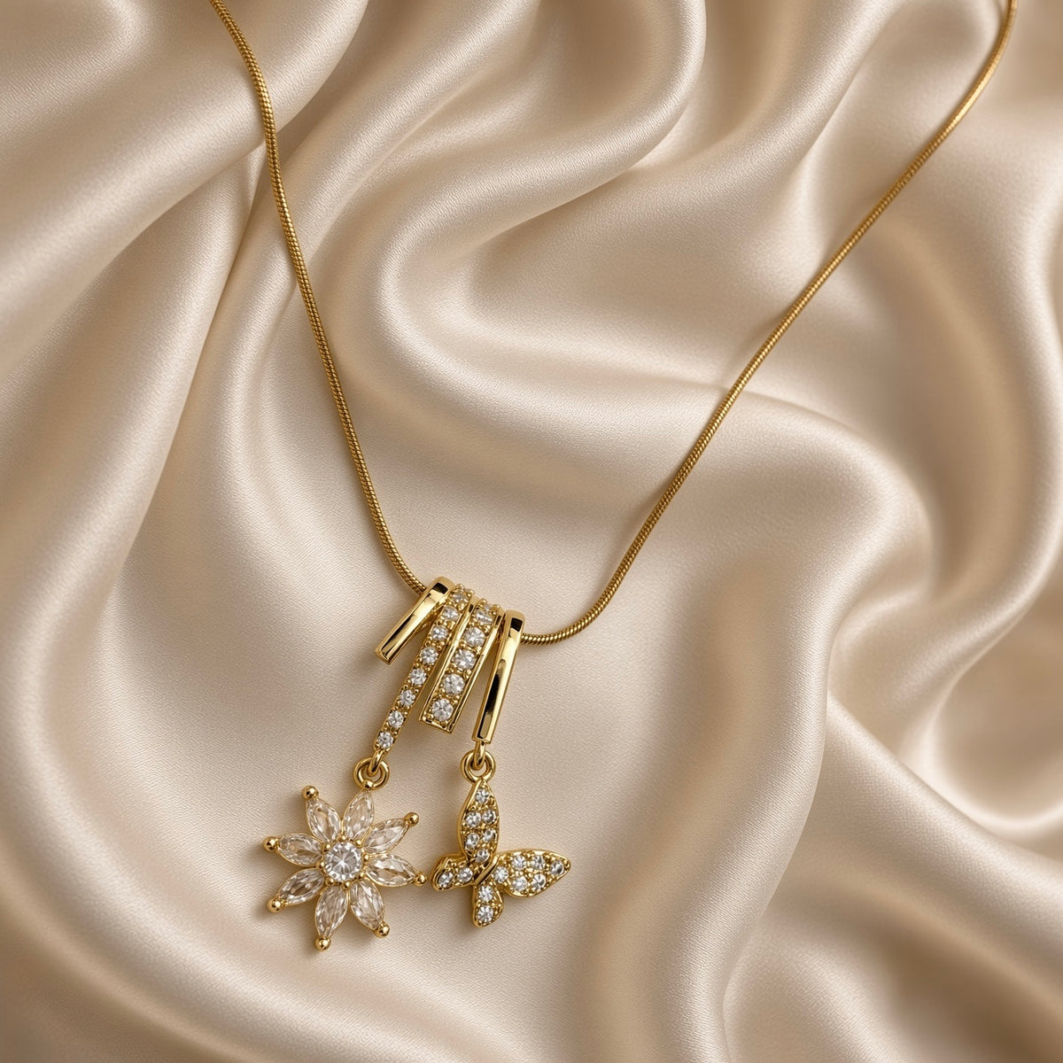 Close-up of gold-tone necklace with clear stone flower and butterfly pendant on cream satin