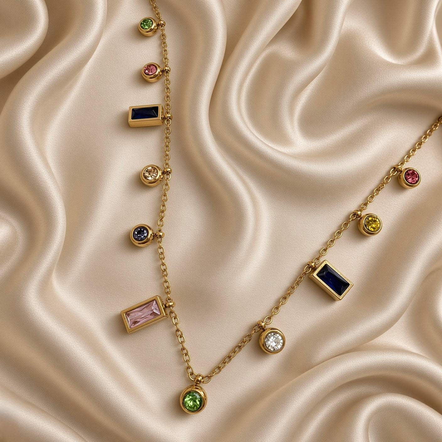 Gold-tone station necklace with multicolour round and rectangular stone-look charms laid on cream satin