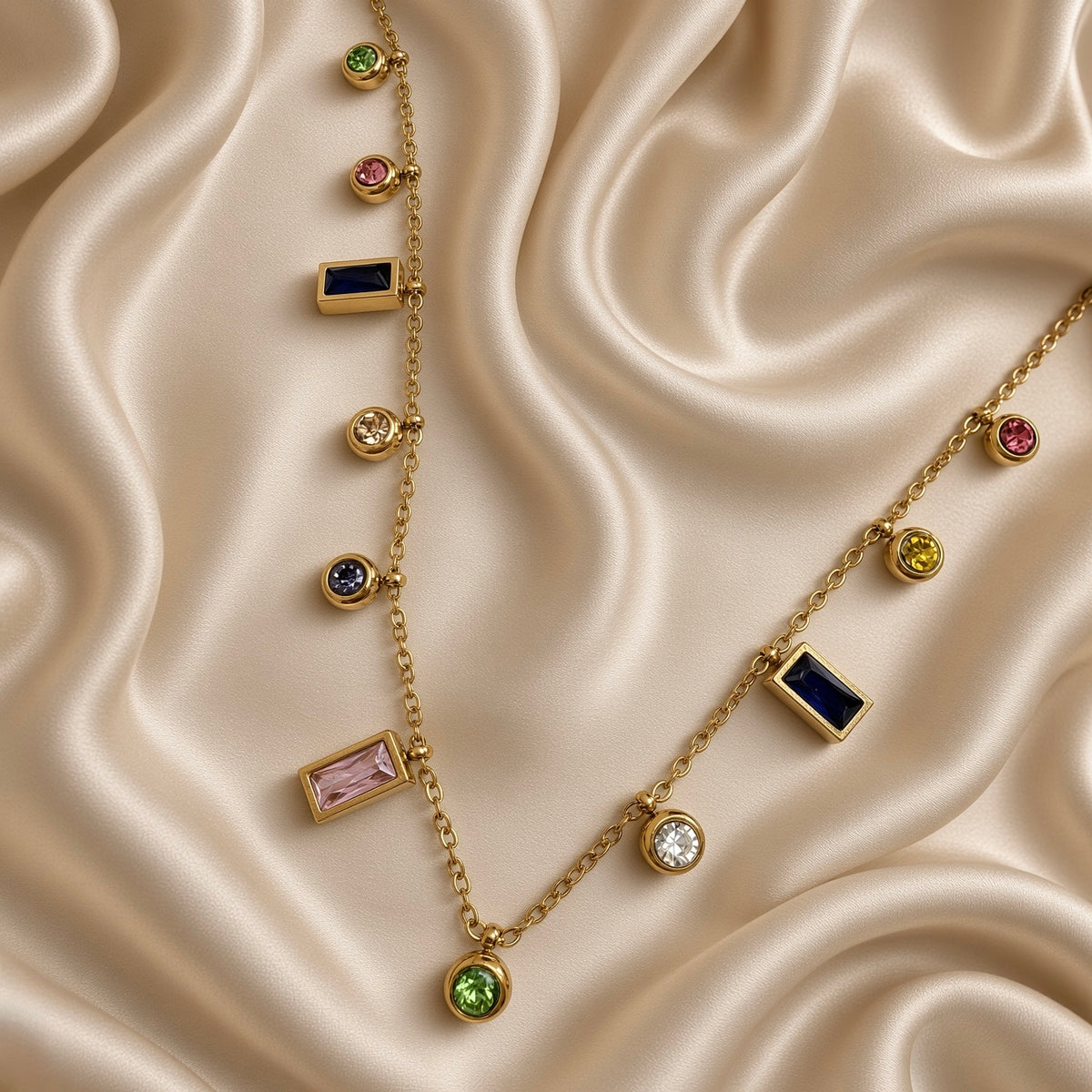 Gold-tone station necklace with multicolour round and rectangular stone-look charms laid on cream satin