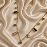 Gold-tone station necklace with multicolour round and rectangular stone-look charms laid on cream satin